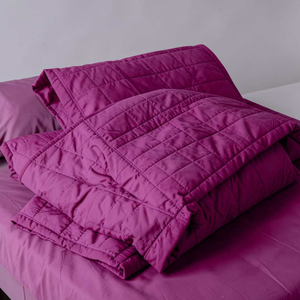 Soft organic cotton quilt set in gentle blush and cream tones, draped across a bed in warm natural light