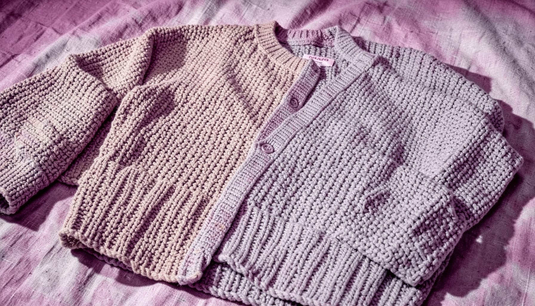 Chunky knit cardigans in oatmeal and dove grey, layered over a linen surface with soft shadows